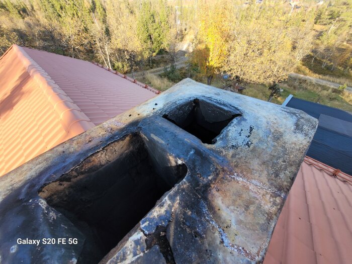 Bilden visar en skorstenstopp med utkragning på ett tegeltak, omgiven av träd.