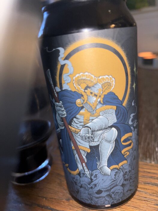 Burk av Foehammer Holy Goat Brewing med detaljerad illustration av riddare på etiketten, stående på ett träbord.