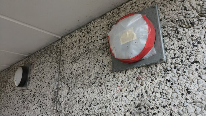 Gatubelysning med provisorisk täckning, tejpad med röd tejp mot en krossad stenfasad.