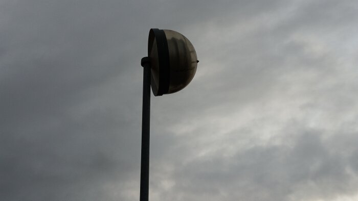 Gammal gatubelysning mot molnig himmel, diskussion om energieffektiva armaturer och kommunala renoveringar.