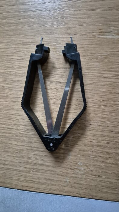 Verktyg för att ta bort IC-kretsar med ben ur hållare, med svart plast och metallarmar, ligger på ett trägolv.