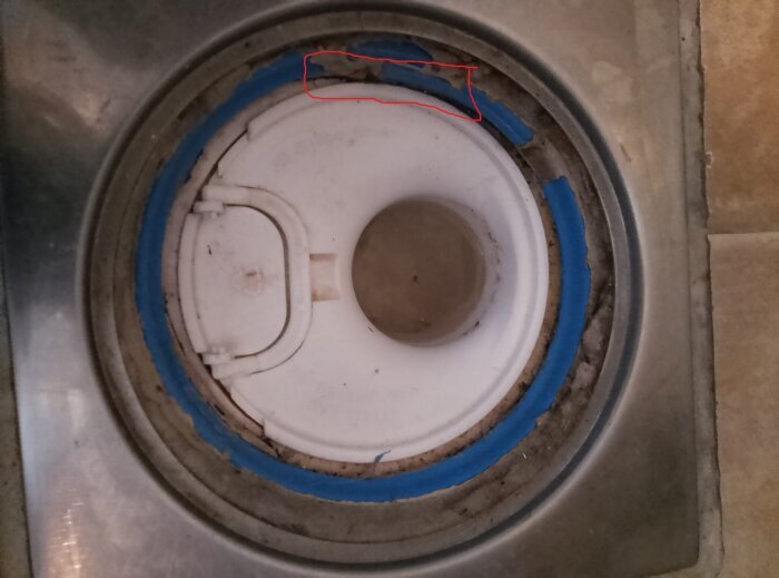 Närbild av avlopp med klämring, delvis omgivet av blå tätning. En fråga om användning av cement vid installation diskuteras.