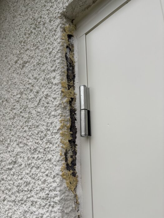 Nyinstallerad vit ytterdörr med gulnad fog och synliga lekablock längs dörrkarmen mot en putsad vägg.