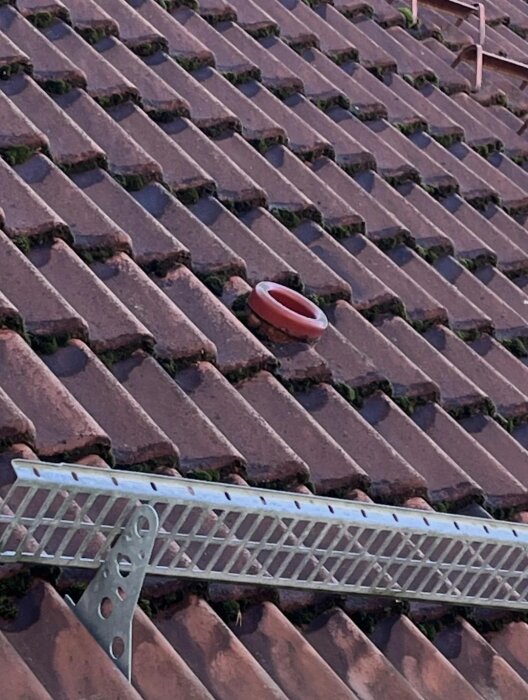 En ventilationsrör installerad genom ett tak med tegelpannor, med en stege fäst framför rören på taket.