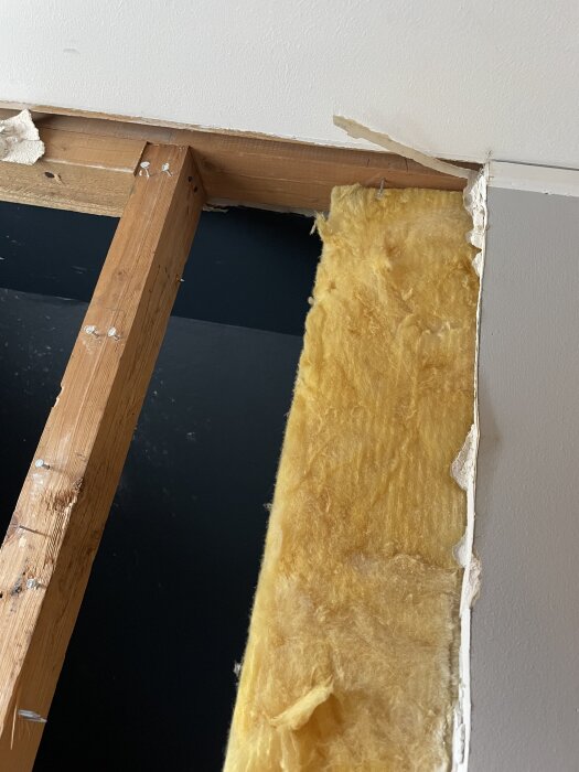 Träregelstruktur och gul isolering i vägg där dörrkarm har tagits bort, synlig nivåskillnad mellan regel och tak.