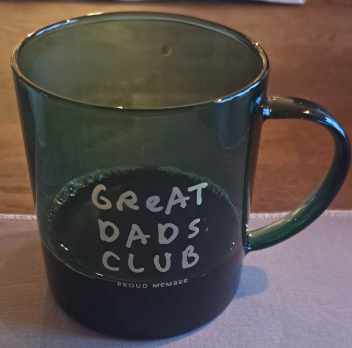Grön mugg med texten "Great Dads Club, Proud Member" på bordet.