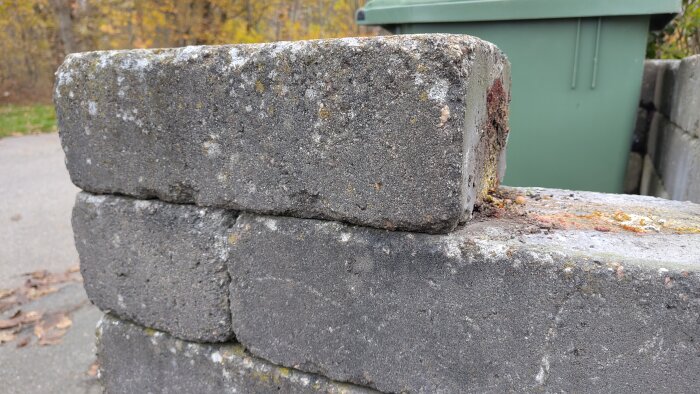 Limmad mur av betongblock bredvid en grön soptunna, problem med att få loss stenarna nämns i forumdiskussionen.