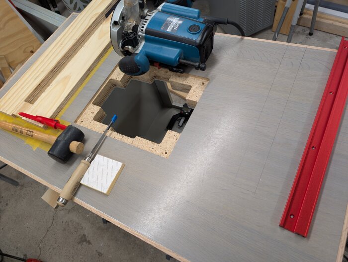 Routerbord med spår för skenor, omgivna av verktyg som hammare och mejsel, samt en blå och röd färgad yta.