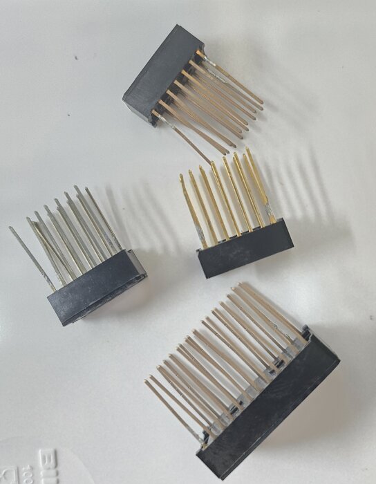 Fyra svarta kontakter med långa metallpinnar placerade på en vit yta.