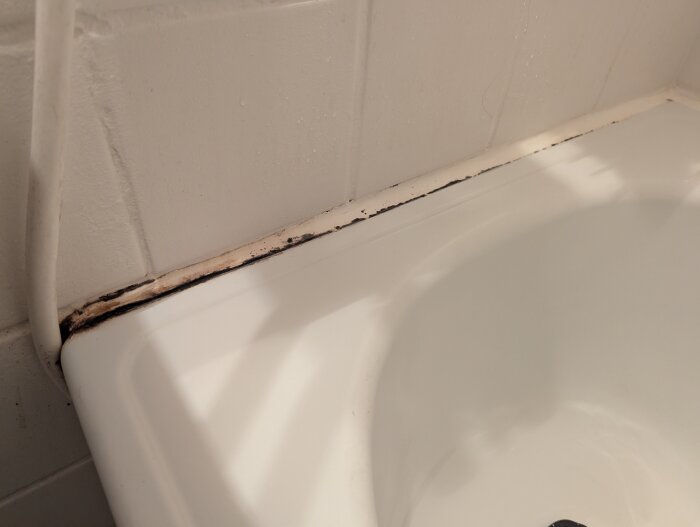 Nedsmutsad silikonfog mellan vit badkar och vägg i ett badrum, visar slitage och fuktproblematik.