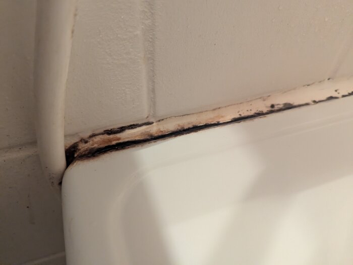 Fog av silikon mellan badkar och vägg med svarta missfärgningar, troligen orsakad av droppande kran.