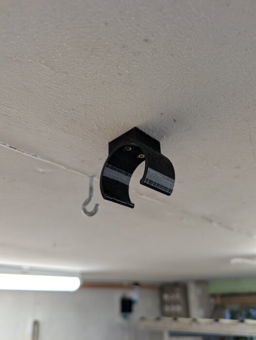 3D-printad hållare monterad i taket för att fästa en slang, med en krok bredvid, i en verkstadsmiljö.