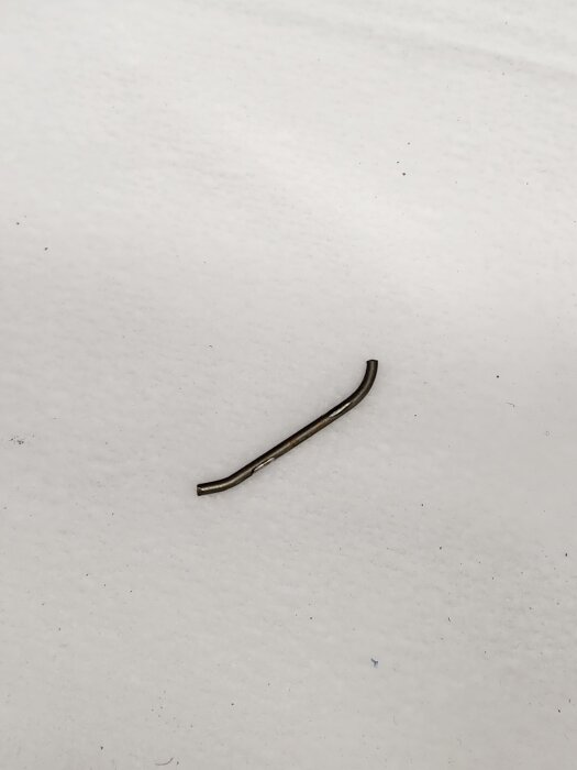 Bruten fjäder från bilens backkamera, avlång och böjd, placerad på en ljus yta.