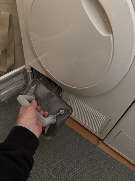 Hand tar ut ett dammfilter från en torktumlare för rengöring.