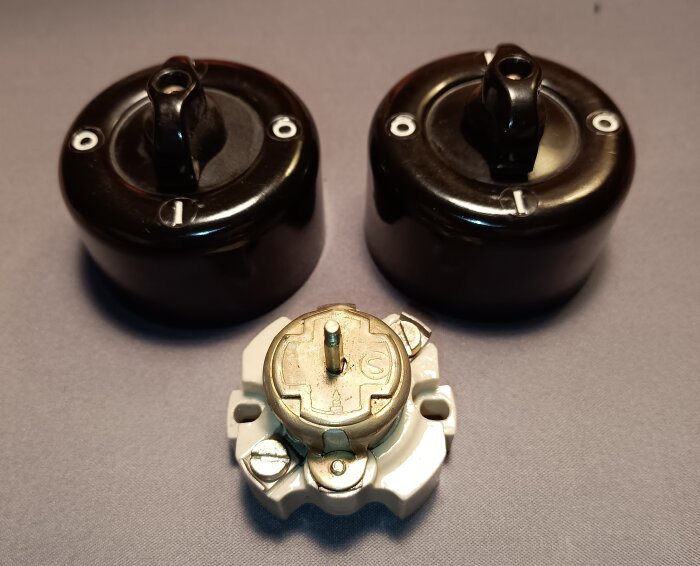 Gammal modell av utanpåliggande brytare i bakelit och porslin, max 15 A, med två svarta brytare och en vit porslinsdel.