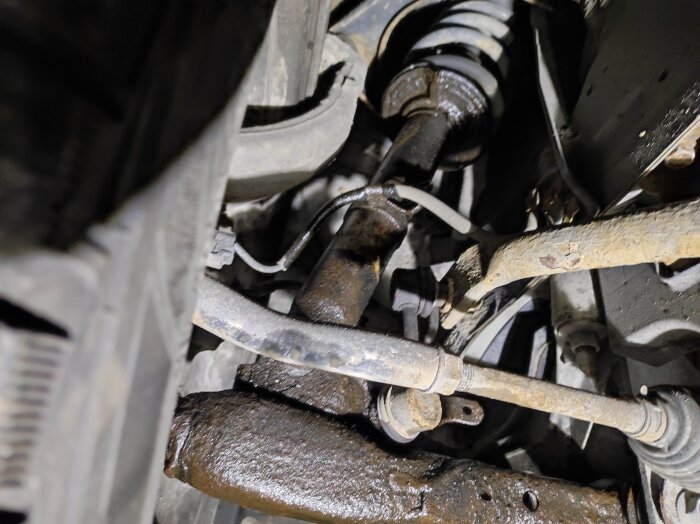 Närbild på bilens framvagn med en läckande stötdämpare på höger sida, tecken på oljeläckage och rost på delarna.