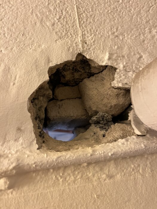 Skadad betongvägg med synlig spricka och eventuella asbestrester under en eternitkanal.