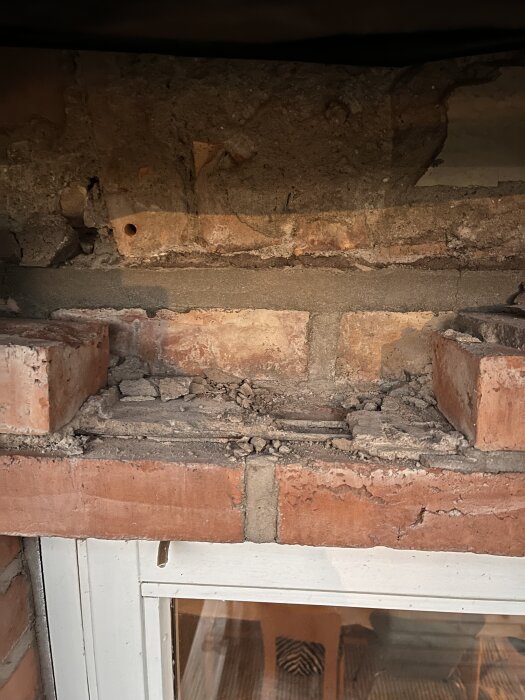 Murad fasad med tegel ovanför ett fönster. Tegel har tagits bort, och ett gammalt tegelvalv syns. Frågetecken kring om hålet breddats med ny balk.