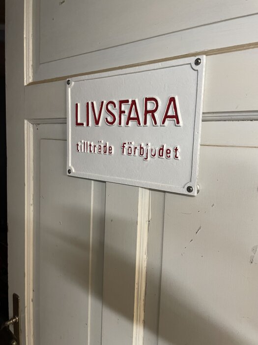 Innerdörr med en skylt som varnar för livsfara och förbjuder tillträde, i ett snickeri där motorcyklar ska förvaras.