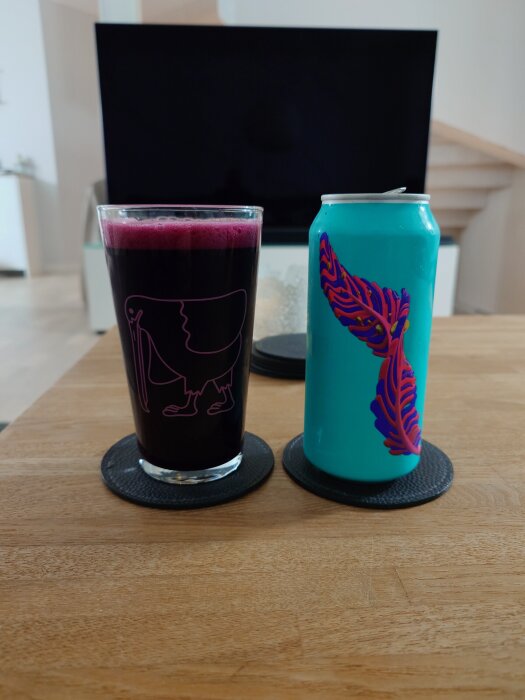 Glas med blåbärssuris och Omnipollo-burk med färgglad design på ett bord.