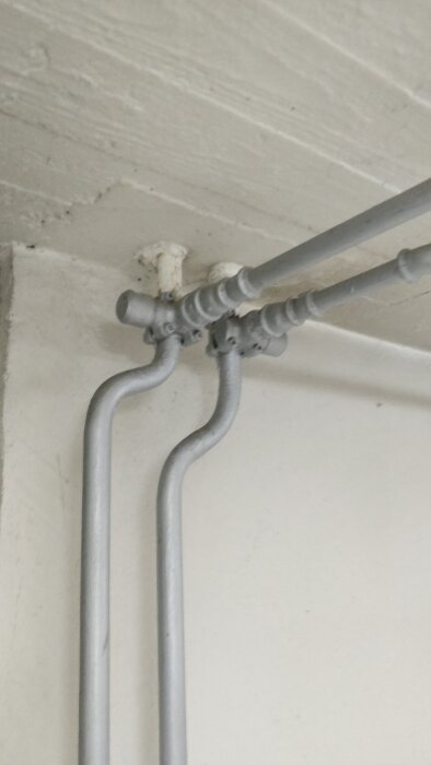 Målade rörkopplingar i en källare med utstickande cylindrar, märkta med "PN25", som ansluter till en radiator som inte blir varm.