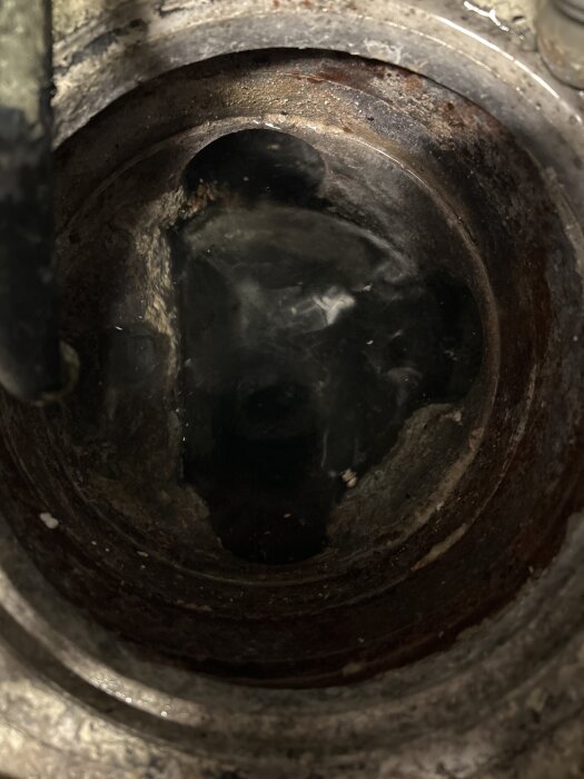 Golvbrunn i källare under rengöring med vatten och avlagringar synliga, omgiven av smuts och rost.