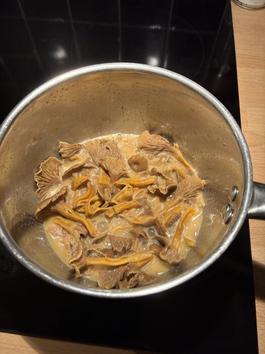 Svamprisotto tillagas i en kastrull på en spis, synliga bitar av gula kantareller och krämig sås.