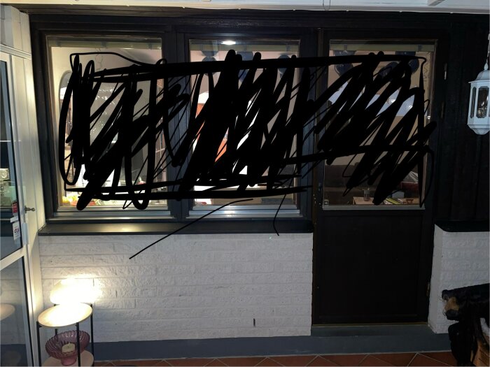 Fönster och dörr på lättbetonghus med vit tegelvägg under, belysning intill väggen.