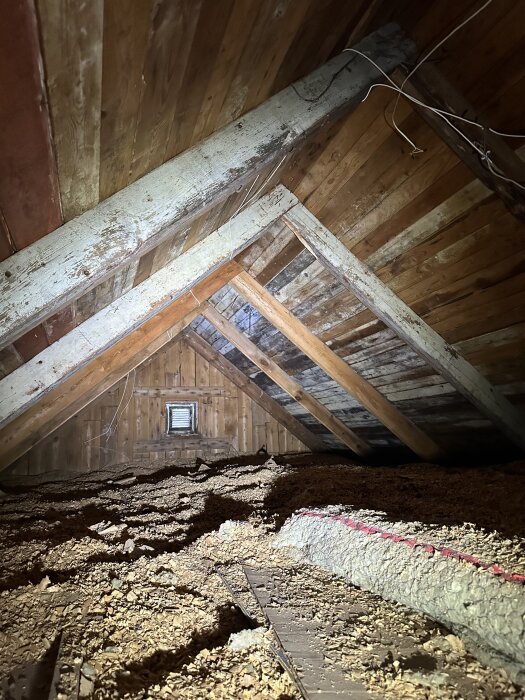 Vindsutrymme i ett gammalt hus med träbjälkar, träpaneler och isoleringsmaterial. Möjliga tecken på vitmögel finns.
