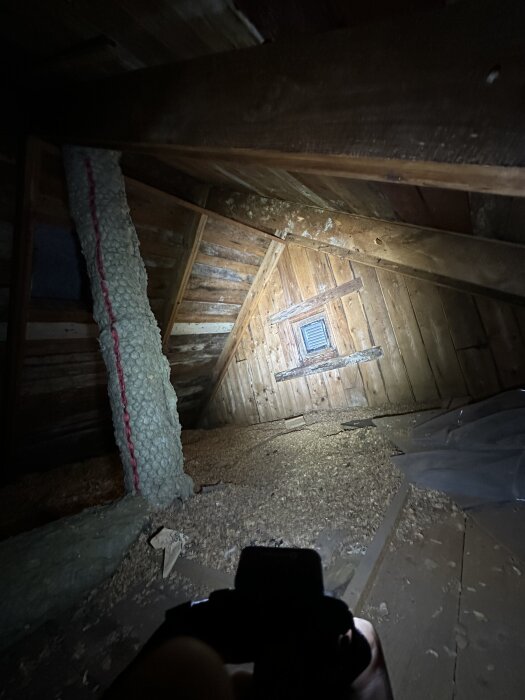 Gammal trävind med isolering, synlig vitmögel på träbalk, fönstergaller i bakgrunden; ficklampa lyser upp trägolv och brädvägg.