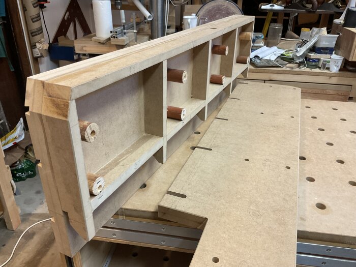 Högt anhåll av trä i verkstadsmiljö, med rundstavsförstärkningar och torsion box-konstruktion, placerat på arbetsbänk. Verktyg och material synliga i bakgrunden.