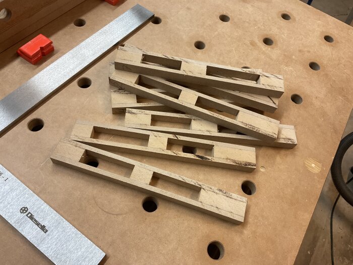 Trästycken med utskärningar på en arbetsbänk, del av ett uppdaterat anhåll för justersåg.