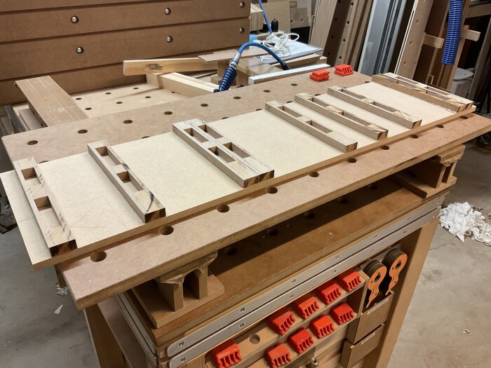 Träbänk med horisontella förstyvningar i MDF under arbete i verkstad; tvingar och verktyg syns i bakgrunden.