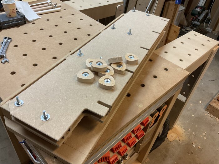 Ett uppdaterat högt anhåll för en justersåg visas på en arbetsbänk, med flera handgjorda trävred för montering.