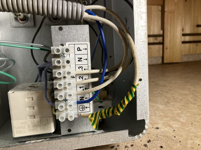 Anslutningsbox inuti bastuaggregat med synliga elledningar och terminaler för två faser, noll och jord.