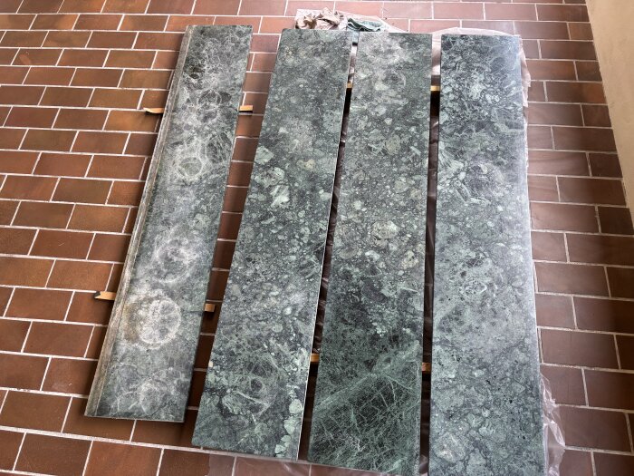 Fyra marmorliknande gröna fönsterbrädor med cirkulära märken, placerade på ett rött klinkergolv.