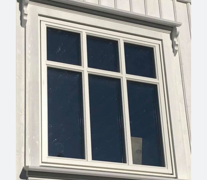 Vitt fönster med mellanliggande spröjs i kryssmönster på vitmålad fasad.
