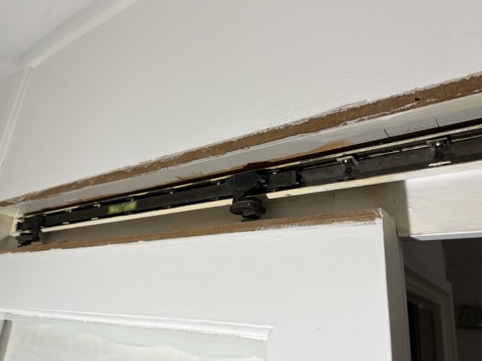 Skjutdörrsskena och hjul under en överliggare, del av en renoveringsfråga om av- och påhakning av dörren.