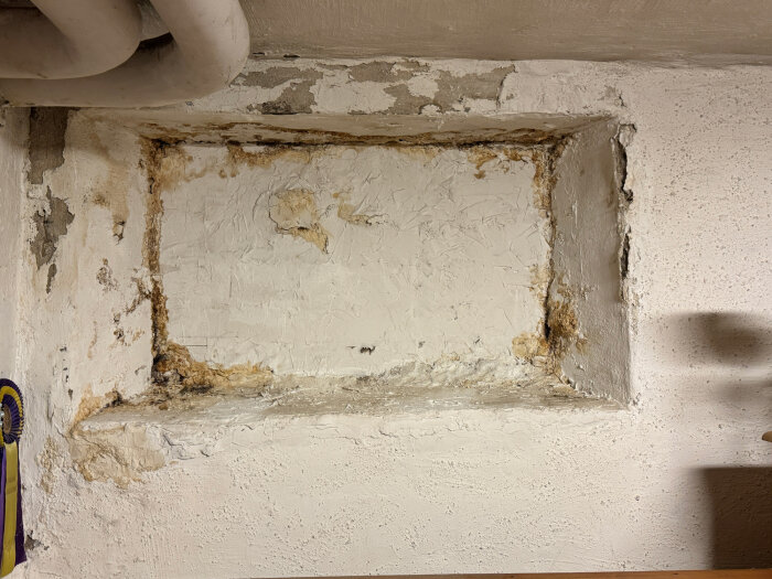 Igenmurat källarfönster med skadad puts, synliga fuktfläckar i hörnen och ovanför, i ett 20 år gammalt hus vars altan skapades av tidigare ägare.