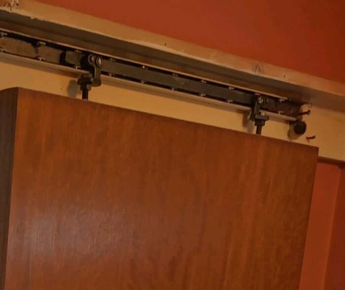 Skjutdörr från 60-talet monterad i en skena med svarta muttrar, del av ett byggprojekt för att flytta dörrens position och vända riktning.