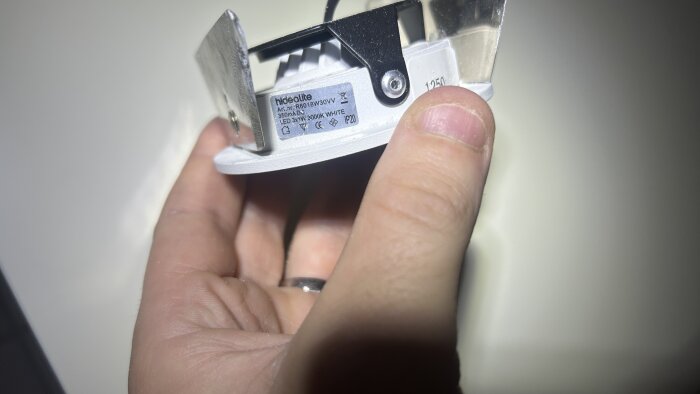 En hand håller en vit Hidealite LED-downlight med specifikationen 350 mA och 3000K, märkt "R6018W30VV", sedd från sidan.