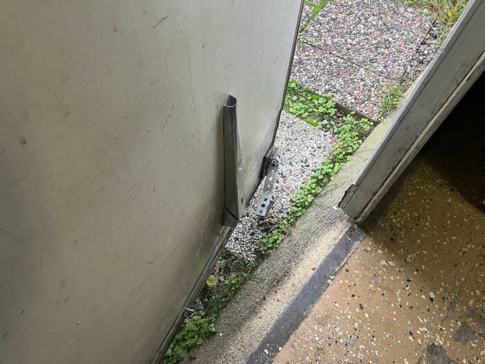 Dubbeldörr i källare med stora glipor längs golvet. Synligt yttre område med plattor och grus. Problem med tätning och isolering.