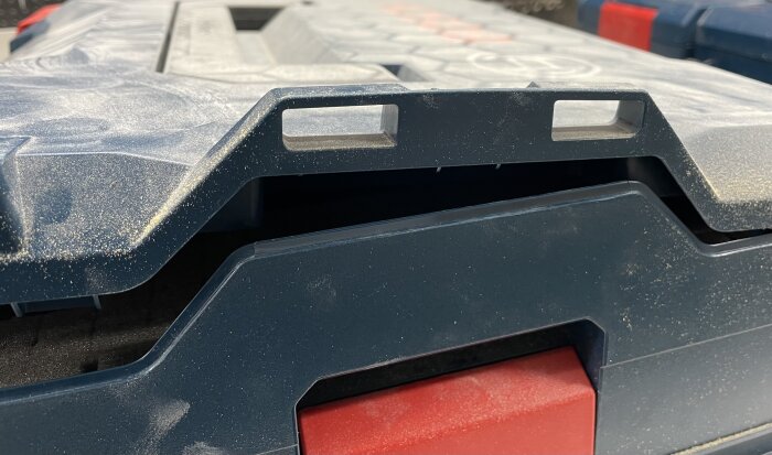 Närbild på verktygslåda med sanddamm och nya fästen i locket, blå plast med röd detalj.