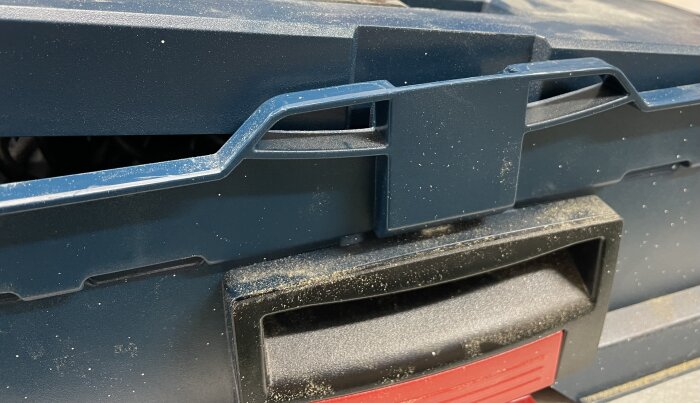 Närbild av blå låda med fästen på locket och svart-rött handtag.