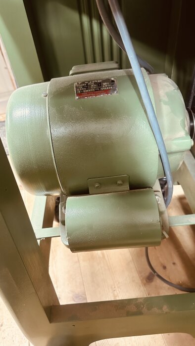 Grön enfasmotor med tydligt gammal etikett på en Ulmia tallriksslip, monterad på ett golv.