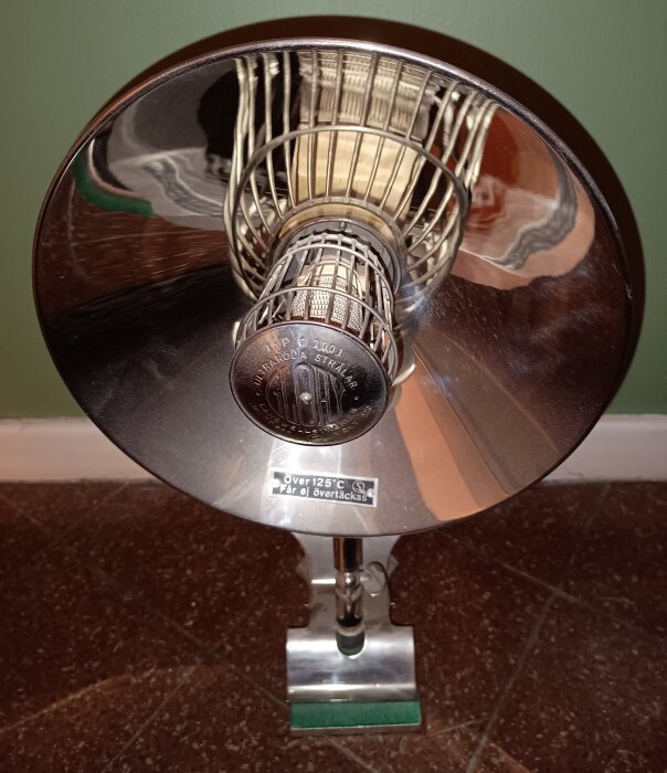 En tidstypisk lampa med metallisk armatur och ett varningsmärke om att den inte får överhettas eller övertäckas.