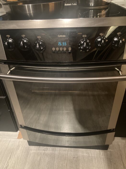 Svart och silverfärgad ugn eller spis med flera vred och digital display som visar tiden 15:55.