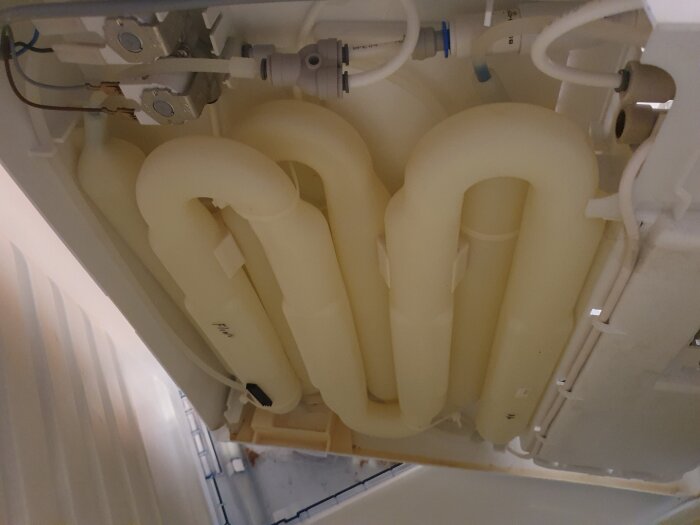 S-formade plaströr som del av kylsystem i ett kylskåp, ovanifrån där rören är anslutna till ventil och kopplingar.