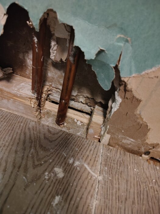 Trasig vägg med exponerade kopparrör, där en del av väggregeln har tagits bort för att ge mer utrymme för rörreparation.