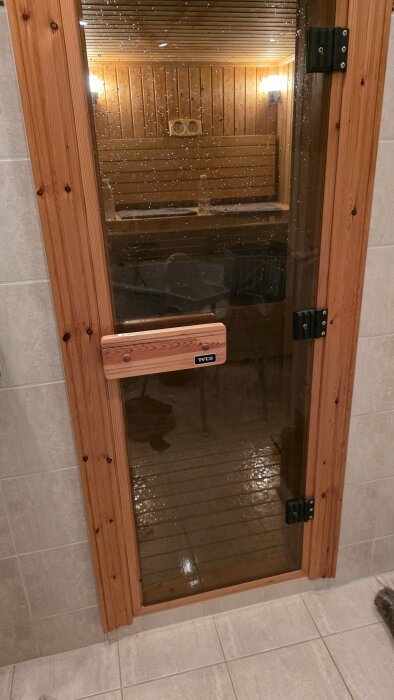 Bastudörr av glas med träram, vattendroppar på ytan och belysning inuti bastun.